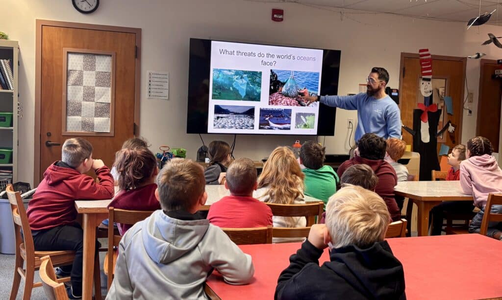 A classroom of students looking at a presentation slide on threats to the ocean