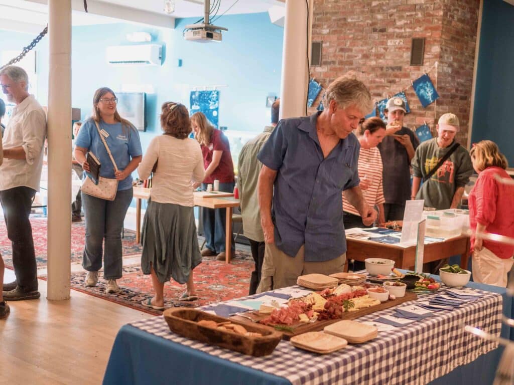 Attendees mingle inside Shaw Institute and one is viewing the charcuterie food display.
