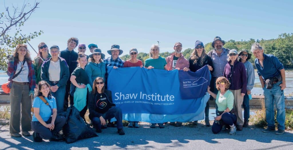 A group of beach cleanup participants pose for a photo while holding a blue Shaw Institute banner