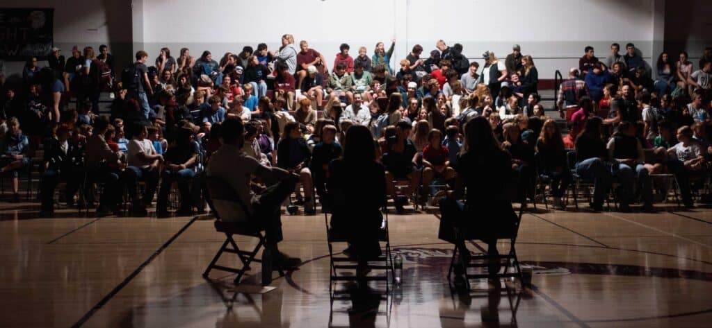 students gathered in assembly for a presentation of three people.