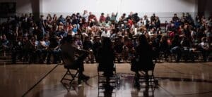 students gathered in assembly for a presentation of three people.
