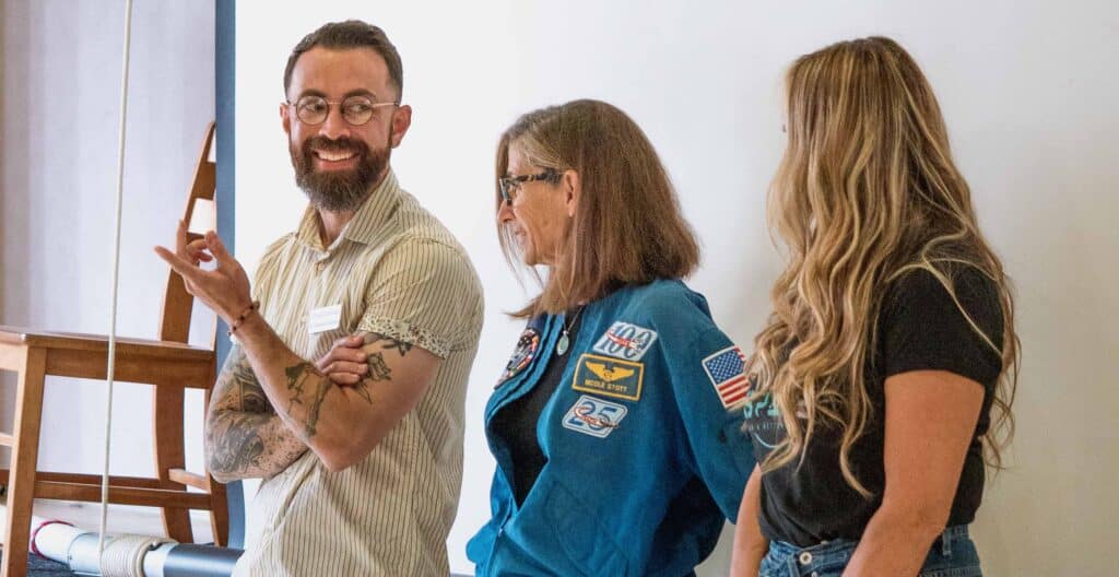 Dr. Charles Rolsky, retired NASA astronaut Nicole Stott, and Christina Korp stand at the front of a class in conversation with each other.