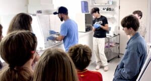 Students watch Dr. Rolsky walk through an experiment under the fume hood in the Shaw Institute lab.