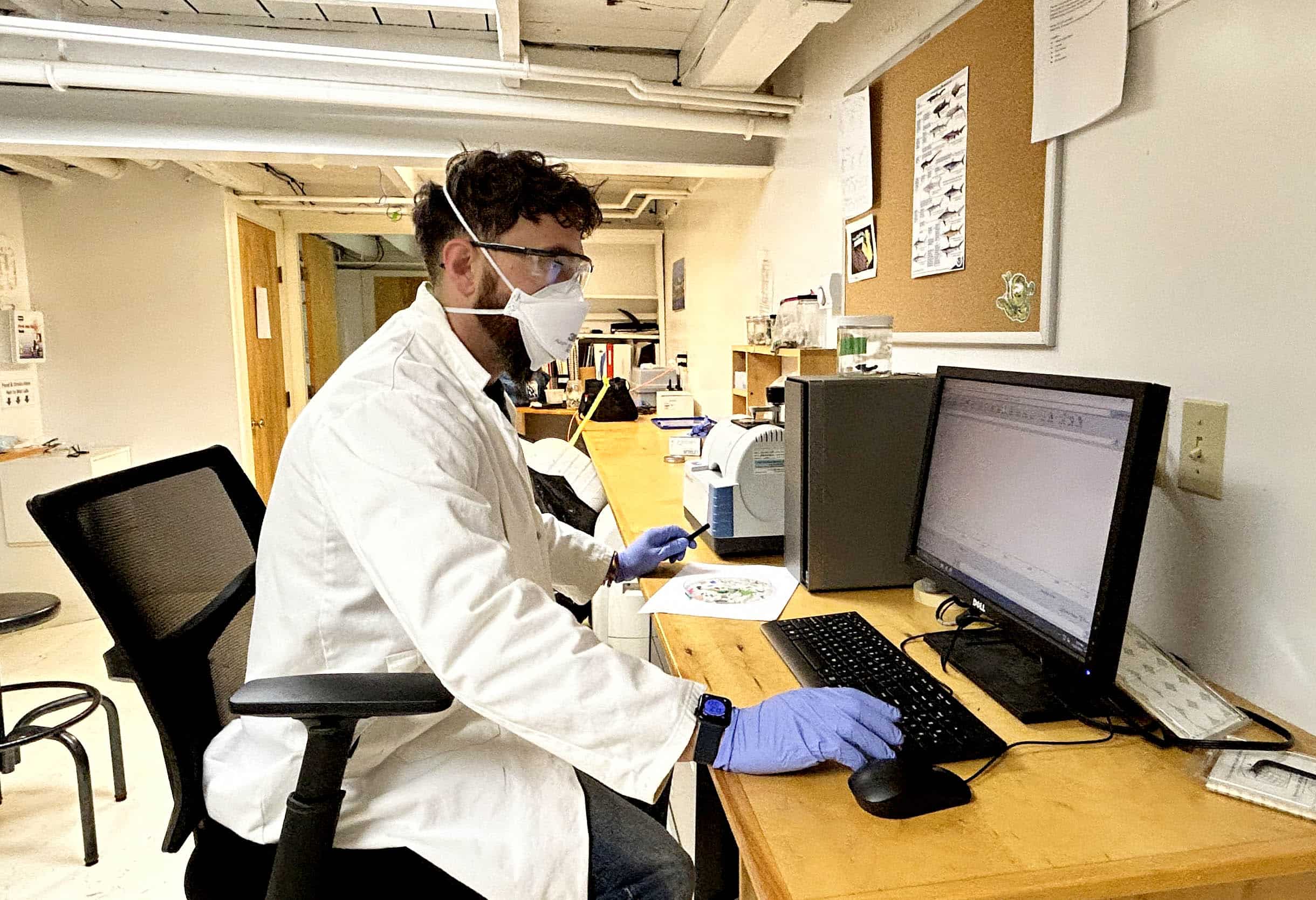 Dr. Charles Rolsky inputs findings into a computer in full PPE while in the lab.